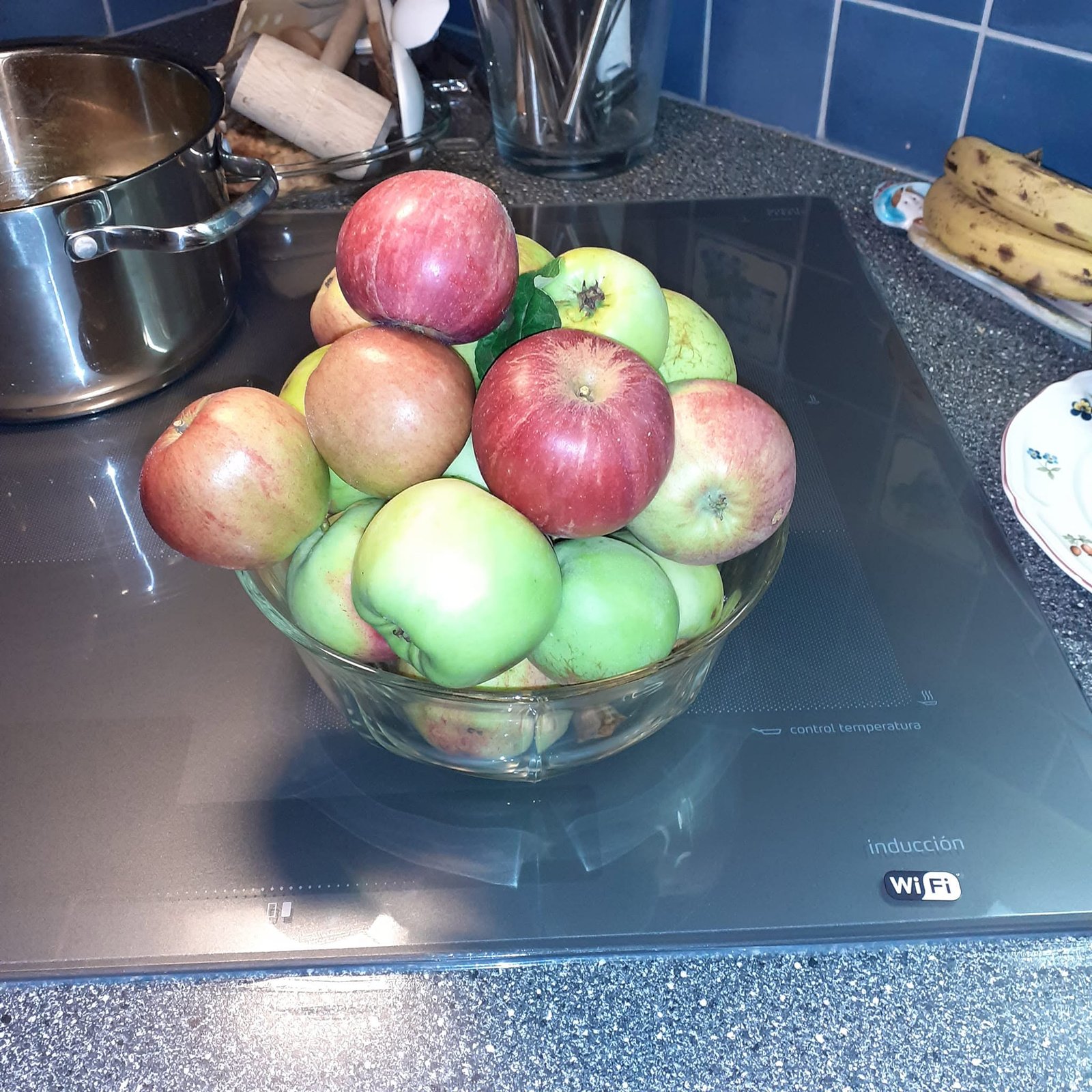 A glass bowl of red and green apples on the kitchen hob